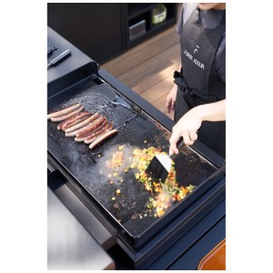 Forge Adour Grillwender im Einsatz: Würstchen und Gemüse werden auf einer Grillplatte gewendet.