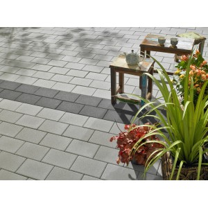 Pavés en béton Vero gris argenté (22,5x15x6cm) à surface fine posés sur terrasse avec table et plantes.