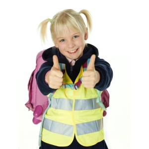 Fröhliches Mädchen mit Kinder-Warnweste Neongelb und Daumen hoch für Sicherheit unterwegs.