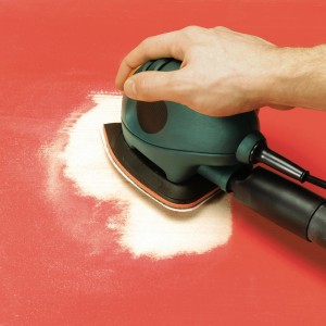 Ponceuse souris Black+Decker avec jeu de patins abrasifs LUX en utilisation sur surface rouge.