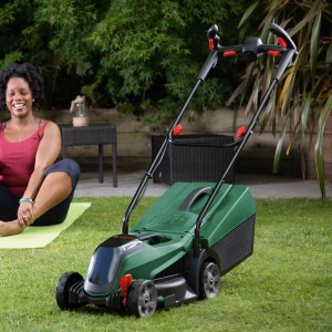 Tondeuse à batterie Bosch CityMower 18V-32 avec batterie et chargeur dans le jardin.