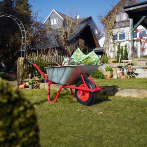 Carriola zincata Pro-Bau-Tec con telaio rosso e vasca da 85 l in giardino.