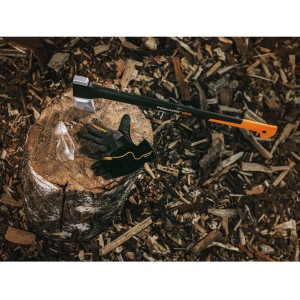 Guanti da giardino Fiskars M, ascia e occhiali protettivi su ceppo di legno, circondati da trucioli.