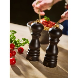 Zwei Paris Salzmühlen aus dunklem Holz mit goldenen Knöpfen auf Holztisch, umgeben von Tomaten und Petersilie. Küchenhelfer.