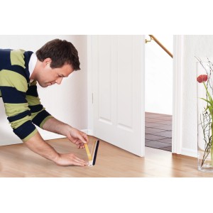 Un homme fixe un joint de porte Tesamoll blanc sur une porte pour sols irréguliers.
