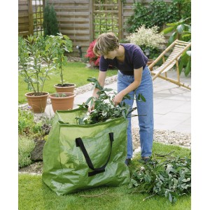 Sac à déchets de jardin vert (245 l) avec une femme le remplissant dans le jardin.