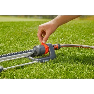 Arroseur oscillant Gardena Aqua M en utilisation : une main ajuste l'arroseur sur la pelouse.