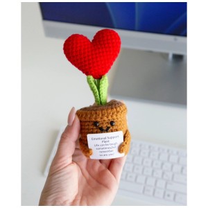 Portafortuna Positive Plant all'uncinetto con cuore rosso nel vaso, tenuto in mano, con messaggio.