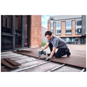 Uomo che lavora con avvitatore a percussione Bosch GSB 18V-65 Solo su una terrazza in legno.