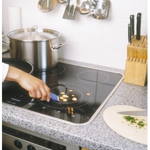 Grattoir universel LUX utilisé sur une plaque vitrocéramique pour enlever les résidus alimentaires.