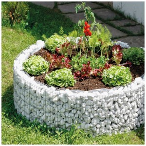 Aiuola rialzata rotonda in gabbioni (Ø 72-92 cm) riempita con pietre bianche, piantata con lattuga e pomodori.