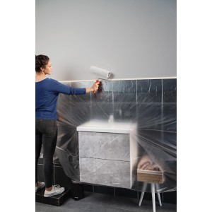 Femme peignant un mur avec le film de masquage Tesa Easy Cover. Protection contre les éclaboussures de peinture lors de la rénovation.