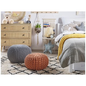 Pouf Conrad en maille cuivrée (Ø 40 cm) dans une chambre à coucher confortable.