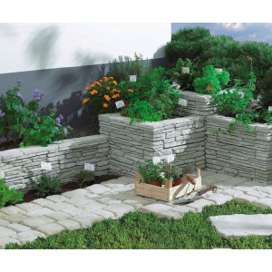 Ziermauer Madoc mit Abdeckplatte in Kalksteinfarben, bepflanzt mit Kräutern und Blumen.