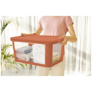 Frau trägt Rotho Aufbewahrungsbox Albris, 45 l, Koralle. Kunststoffbox mit transparentem Deckel.