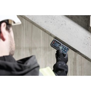 Arbeiter mit Schutzhelm misst mit Bosch Laser-Entfernungsmesser GLM100-36CG eine Betonwand. Grüner Laser für präzise Messungen.