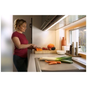 Luminaire LED Osram sous meuble de cuisine : Femme coupant des légumes sous la lumière.