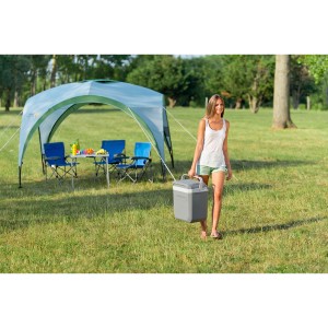 Frau trägt graue Powerbox Plus 24l Kühlbox im Freien. Campingzelt im Hintergrund.