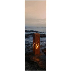 Colonne de feu aspect rouille craquelée, 90cm de haut, avec lumière vacillante sur plage de galets.
