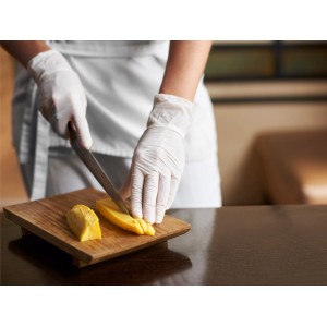 Mani con guanti monouso in lattice bianchi tagliano mango su tagliere in legno. Taglia M, 100 pezzi.