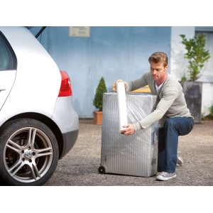 Homme emballant une valise avec du film étirable LUX (0,5 m x 120 m) devant une voiture. Matériau de couverture pour déménagement.