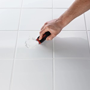 Application de la solution adhésive Ridder Fix n Clean sur des carreaux de salle de bain blancs.
