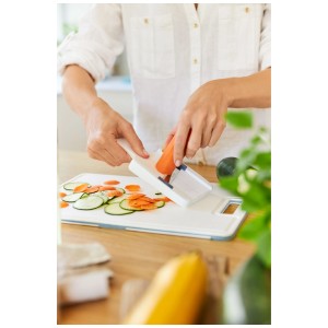 Rotho Râpe à légumes Basic en action : Coupe une carotte en tranches sur une planche à découper.