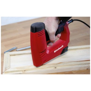 Cucitrice elettrica rossa Einhell che fissa listelli di legno, punti metallici visibili.