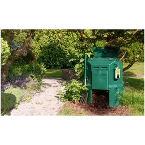 Thermo-composteur vert Handy 250 dans un jardin avec une fourche à compost. Idéal pour le compostage.