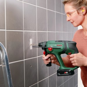 Donna che fora una parete piastrellata con il trapano a percussione a batteria Bosch UniversalHammer 18V.