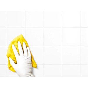Mano con guanto monouso bianco senza lattice pulisce piastrelle bianche con panno giallo.