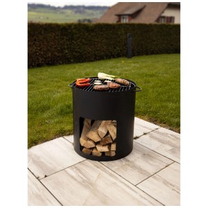 Brasero Nouvel en acier noir avec grille et bois de chauffage dans le jardin.