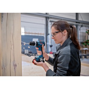 Donna che fora il legno con il trapano avvitatore a percussione a batteria Bosch Professional GSB 18V-90 C.
