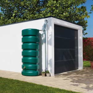 Serbatoio acqua Garantia Classico, 650 l, verde scuro, accanto a un garage. Cisterna per irrigazione giardino.