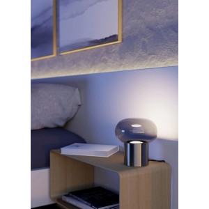 Moderne Tischleuchte Bravino mit leuchtendem Rauchglas und mattem Nickel-Sockel auf Nachttisch im Schlafzimmer.