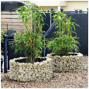 Due aiuole rialzate rotonde in gabbioni (Ø 72-92 cm) con piante su pacciame di corteccia in giardino.